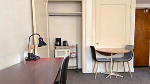 A room with a wooden table, two chairs, a lamp, a coffee maker, and a microwave. - Gold Coast Hideaway | Vintage & Inviting Studio (Chicago)