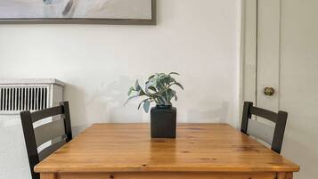 Een houten eettafel met twee stoelen, een kamerplant en een schilderij aan de muur.