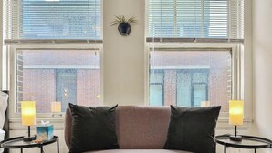 A room with a sofa, two lamps, a small table, and a potted plant. - Chic Studio in the Heart of the Gold Coast (Chicago)