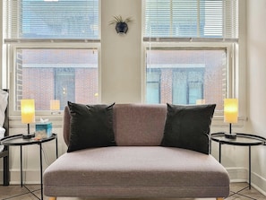 A room with a sofa, two lamps, a small table, and a potted plant. - Chic Studio in the Heart of the Gold Coast (Chicago)