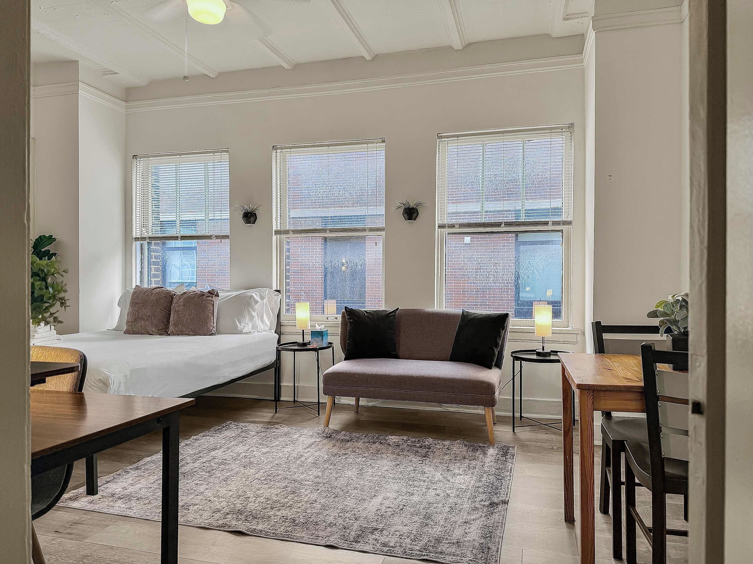 A modern bedroom with a bed, two side tables, a chair, and a dining table.