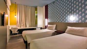 Habitación de hotel con dos camas, un escritorio, una silla y una ventana con cortinas.