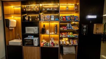 Um minibár compacto com micro-ondas, diversos snacks e bebidas.
