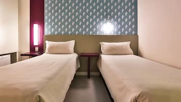 A hotel room with two single beds, a nightstand with a lamp, and a wall with a cactus pattern.