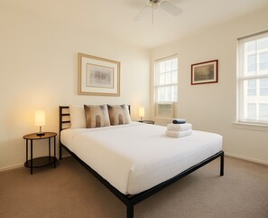 A hotel room with a bed, two bedside tables, a ceiling fan, and two windows. - Stylish Gold Coast 1BR with Vintage Flair (Chicago)