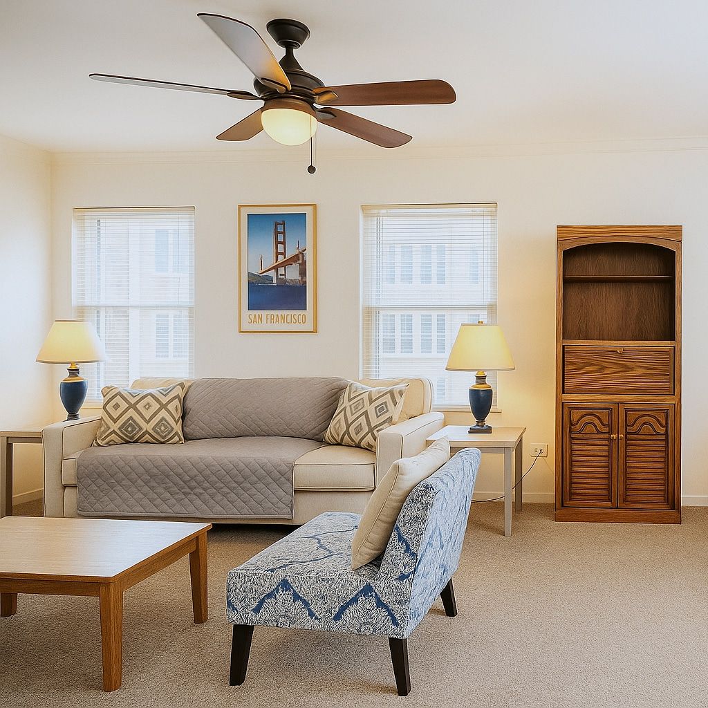 A living room with a sofa, ottoman, coffee table, two lamps, a ceiling fan, and a wooden cabinet.