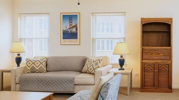 A living room with a sofa, ottoman, coffee table, two lamps, a ceiling fan, and a wooden cabinet.