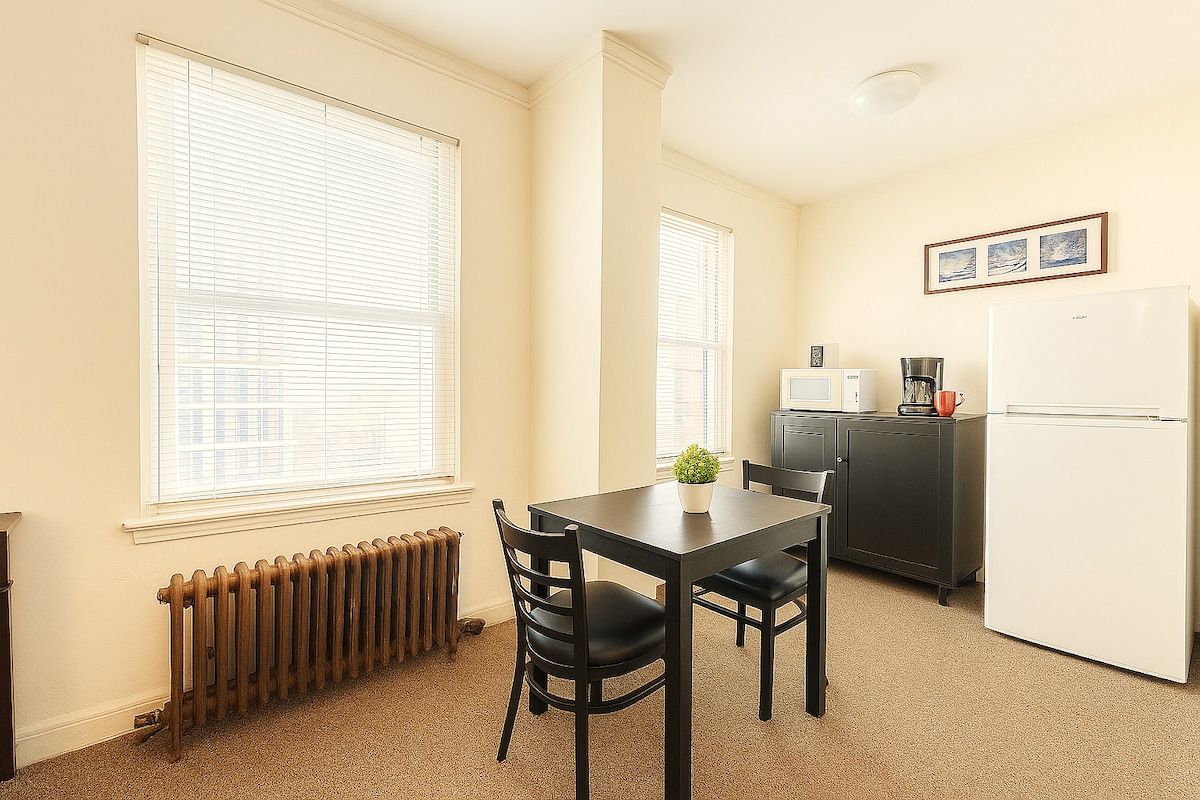 Une cuisine de taille réduite comprenant une table à manger, des chaises, un réfrigérateur et un radiateur.