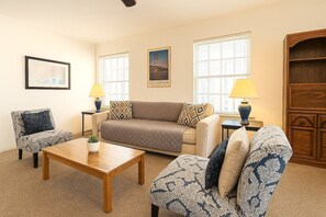 A living room with a sofa, two armchairs, a coffee table, and a lamp. There are two windows with blinds, a framed picture on the wall, and a wooden cabinet. - Stylish Gold Coast 1BR with Vintage Flair (Chicago)