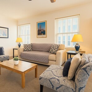 A living room with a sofa, two armchairs, a coffee table, and two lamps. There are two windows with blinds, and a framed picture on the wall. - Stylish Gold Coast 1BR with Vintage Flair (Chicago)