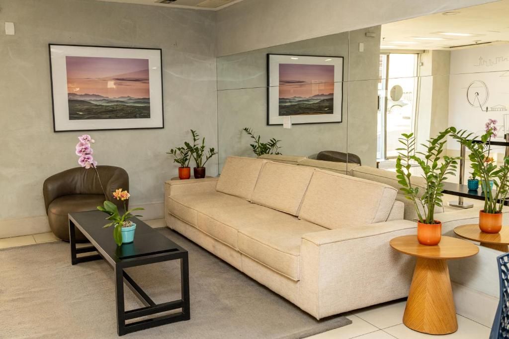 Uma sala de estar moderna com um sofá bege, uma mesa de centro preta e plantas em vasos.