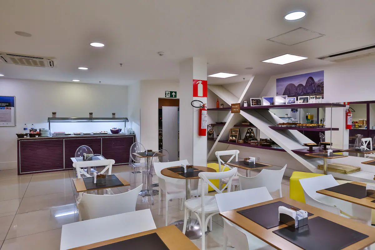Un restaurant moderne avec des chaises blanches et jaunes, un comptoir doté d’une vitrine, et un escalier menant à une mezzanine.
