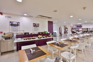 Eine Cafeteria mit Tischen und Stühlen, einer Speisetheke mit Essen sowie Postern an den Wänden.
