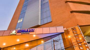 Um edifício alto com design moderno, apresentando uma entrada destacada com portas de vidro e uma placa com a inscrição "NOBLE INN PAMPULHA".