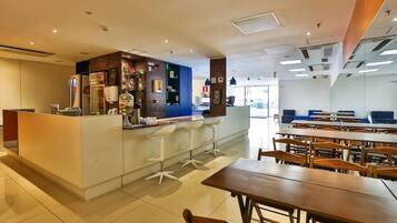 A modern dining area with a central bar, white bar stools, and wooden tables.