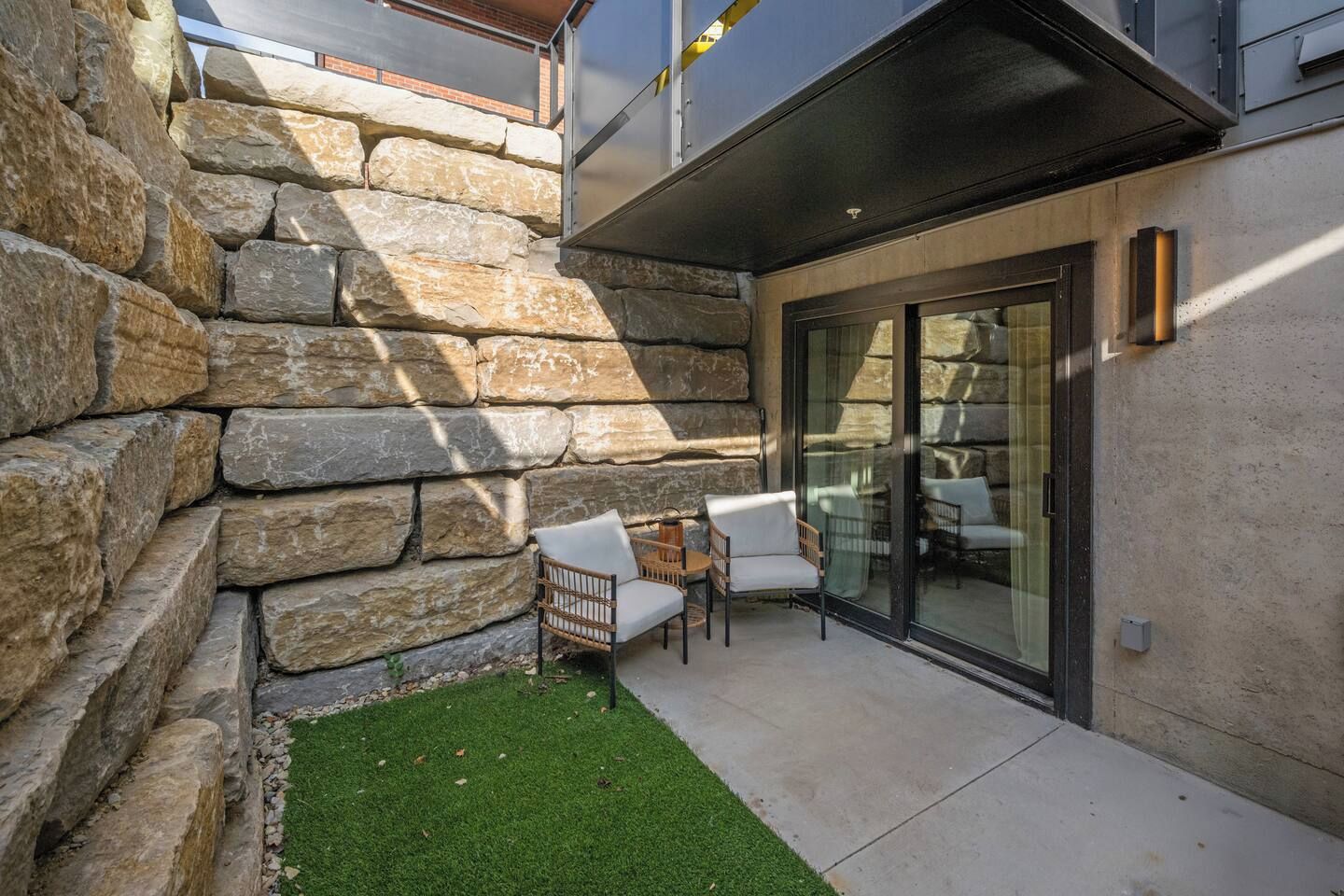 A patio with stone walls, a small lawn, and outdoor seating.