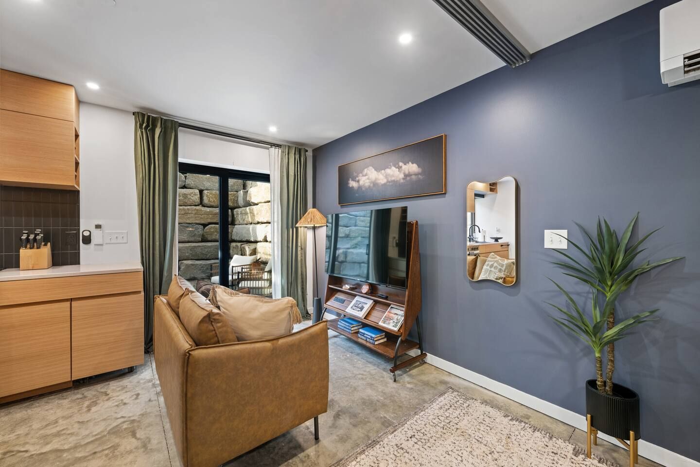 A modern living room with a sofa, a television, a mirror, and a potted plant.
