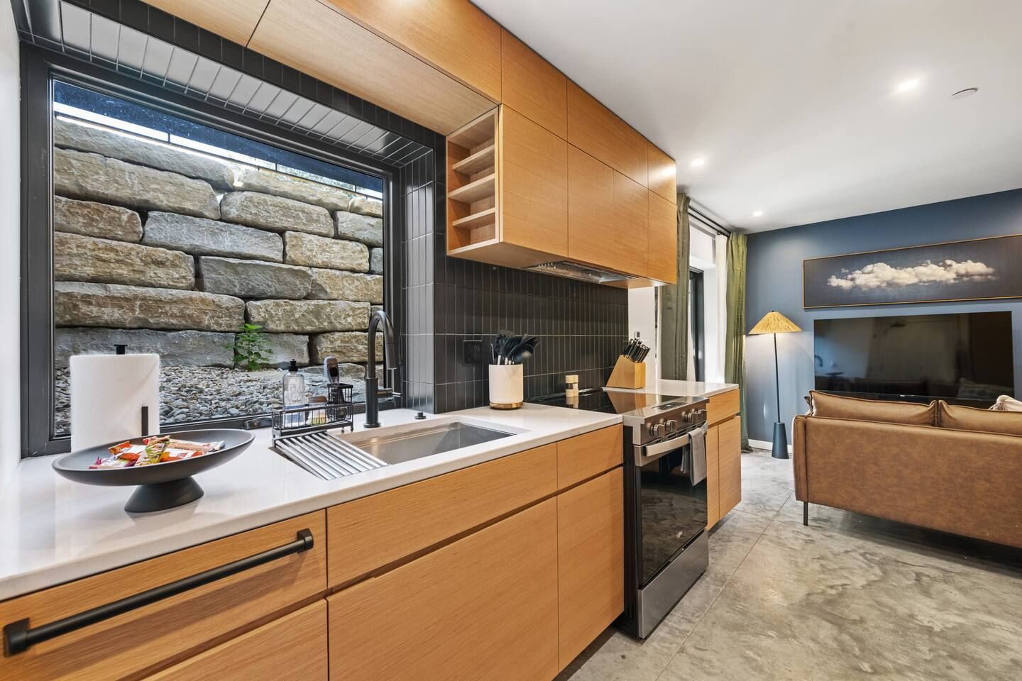 A modern kitchen with a stone wall backsplash, wooden cabinetry, and a built-in oven.