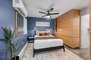 Ein Schlafzimmer mit einem Bett, Nachttischen, einem Deckenventilator, einer Wandklimaanlage und einem großen Kleiderschrank.