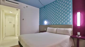 A hotel room with a bed, a nightstand, a wall-mounted light, and a door leading to another room.