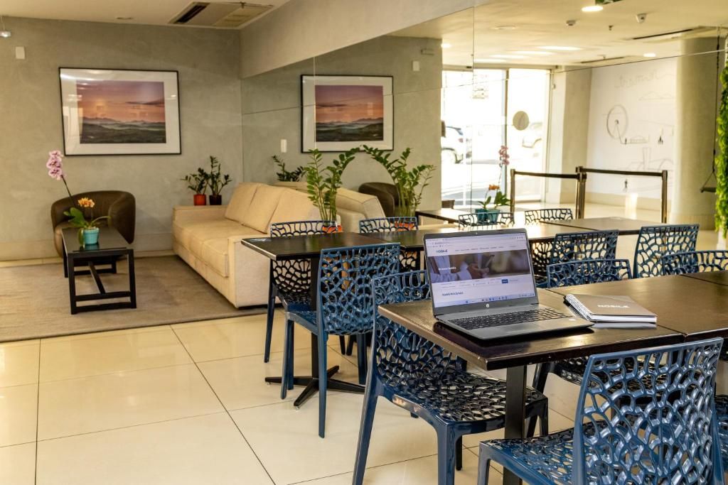 Espaço de escritório moderno com um laptop sobre a mesa, cadeiras azuis, um sofá e duas imagens emolduradas na parede.