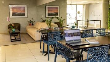 Espaço de escritório moderno com um laptop sobre a mesa, cadeiras azuis, um sofá e duas imagens emolduradas na parede.