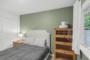 Une chambre à coucher avec un lit, une table de chevet, une commode et une fenêtre avec des rideaux.