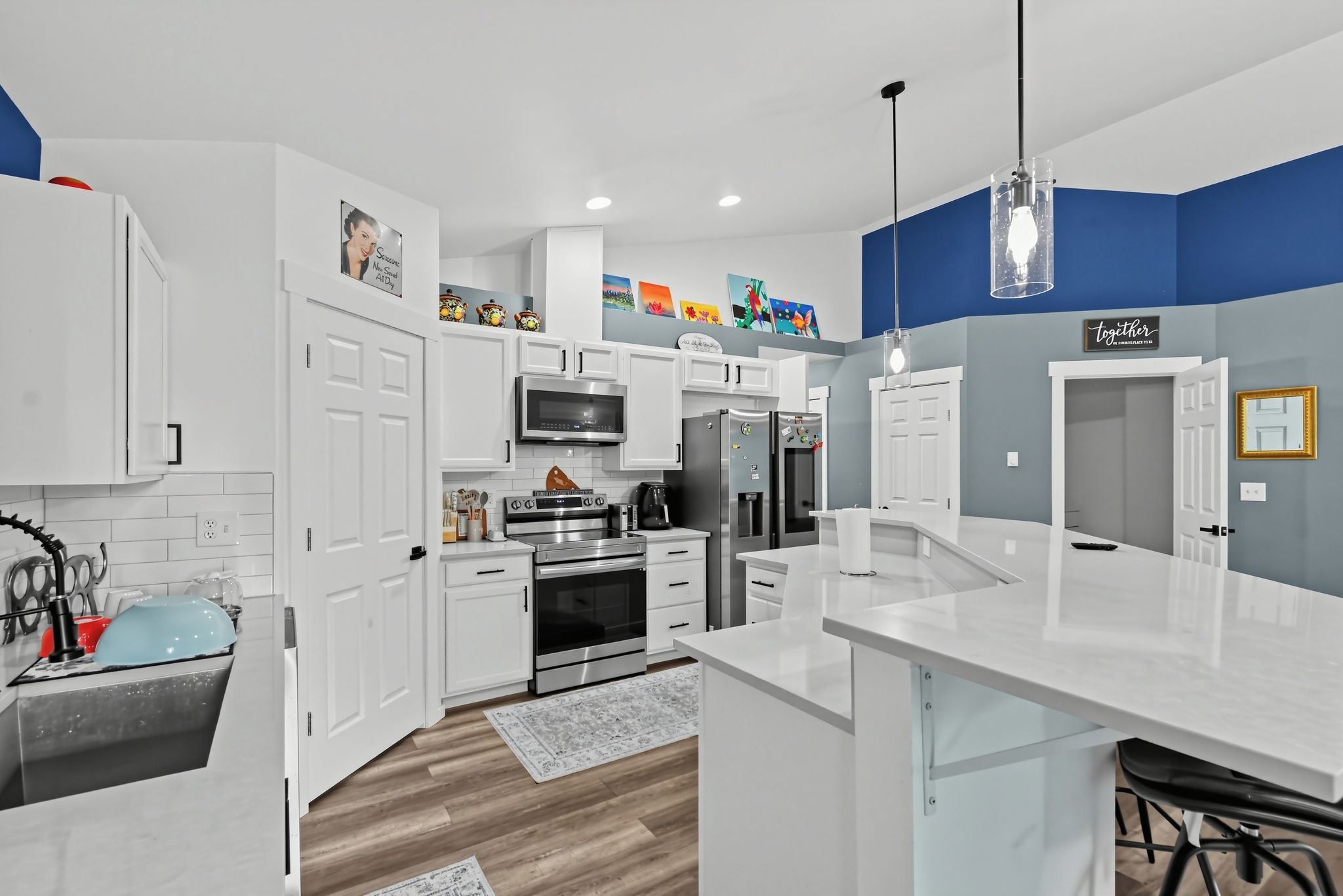 A modern kitchen with white cabinetry, stainless steel appliances, and a blue accent wall.
