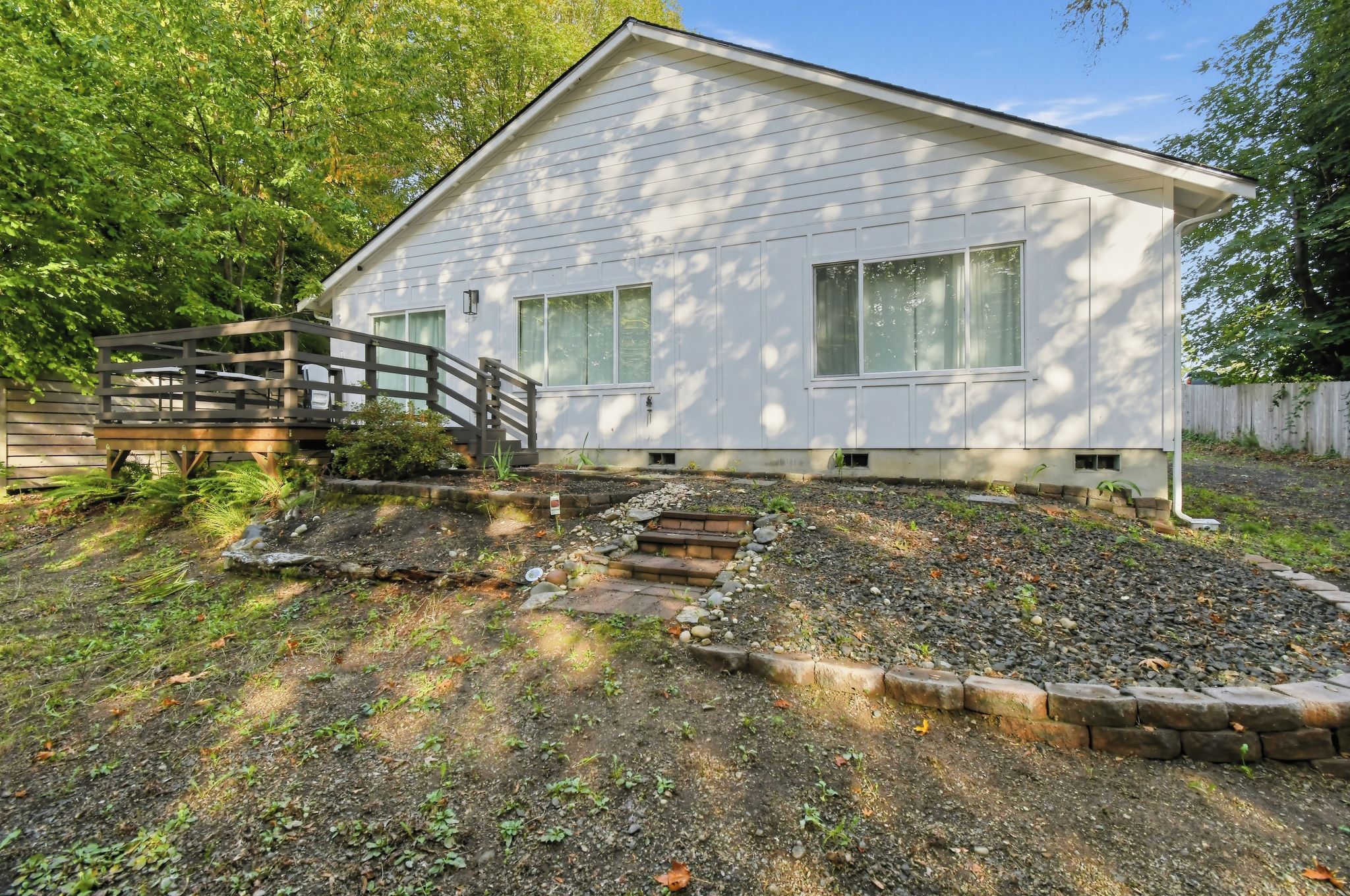 A single-story house with a front porch, a wooden deck, and a garden area with a stone pathway leading to the house.