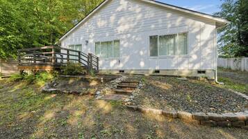 A single-story house with a front porch, a wooden deck, and a garden area with a stone pathway leading to the house.