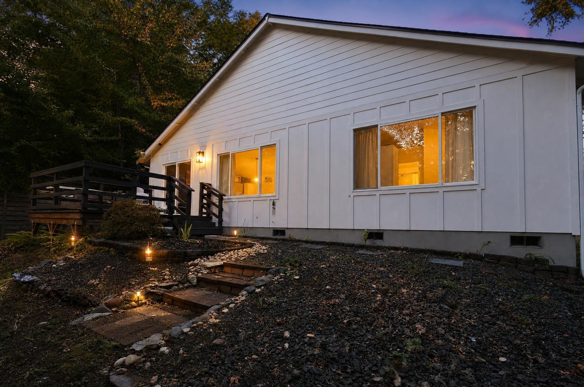 A white house with a wooden deck and a stone pathway leading to the entrance.