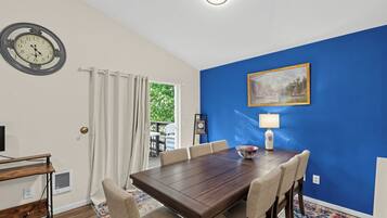A dining area with a wooden table and chairs, a clock, a painting, and a lamp.