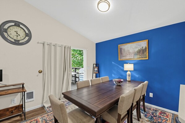 Un coin repas avec une table et des chaises en bois, une horloge, un tableau et une lampe.