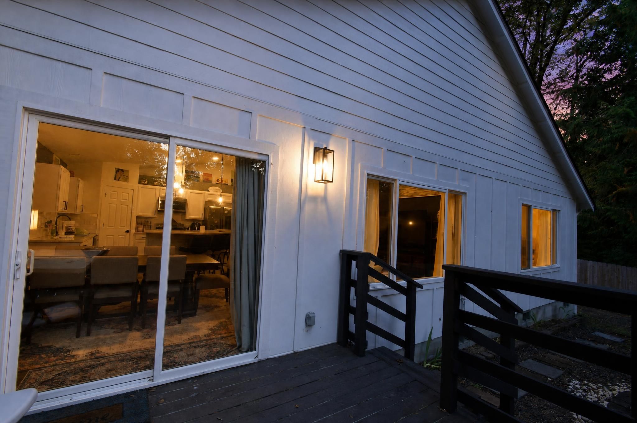 Et hus med en overdækket veranda, et spiseområde med stole, og et køkken, der kan ses gennem glasdøre.