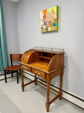 Ein Holztisch mit Schubladen und geschwungener Tischplatte, an einer Wand platziert, über der sich ein farbenfrohes Gemälde befindet.