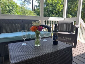 A wicker table with a bottle and glasses, a wicker sofa, and a view of trees.