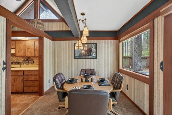 A dining area with a table set for four, wooden cabinets, a chandelier, and a large window.