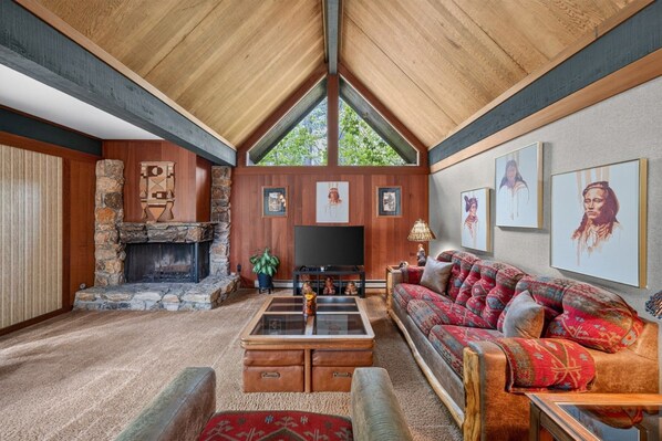 A spacious living room with a stone fireplace, a large television, and a comfortable sofa.