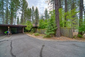 A paved driveway leading to a garage with a covered area, surrounded by tall trees and a wooden fence.