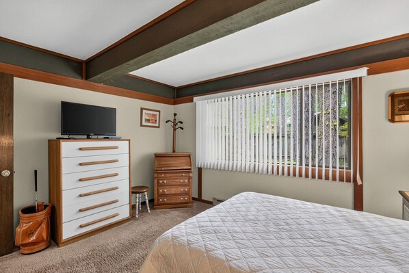 A bedroom with a bed, dresser, television, and a window with blinds.