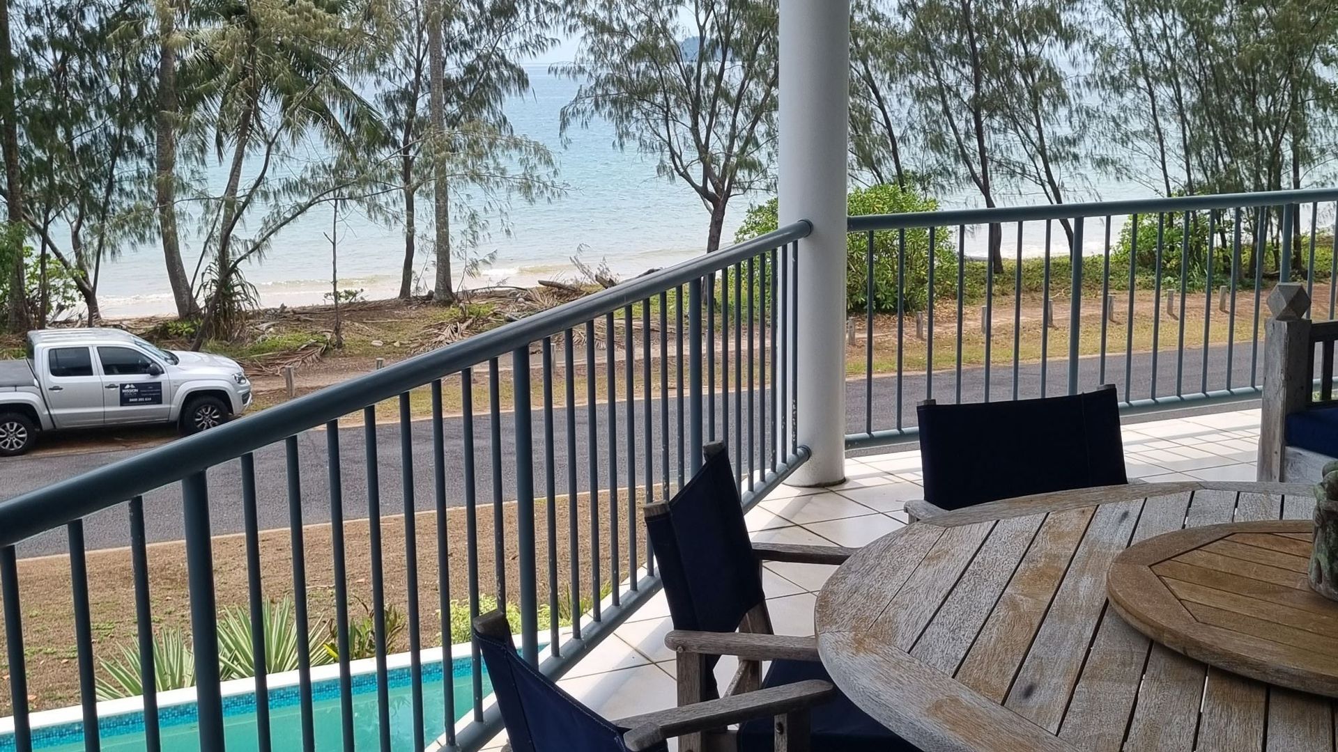 A balcony with a view of the beach and ocean, a pool, and outdoor seating.