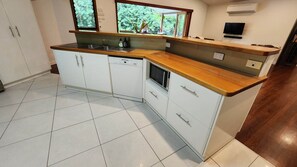 A kitchen with white cabinets, a wooden countertop, a dishwasher, and a window with a view of trees. - The Canopy- Stunning elevated home (Bingil Bay)