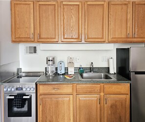 A kitchen with wooden cabinets, a stove, a sink, and various appliances including a coffee maker and toaster. - Free Parking Newly Renovated New Kitchen 4th FL (Honolulu)