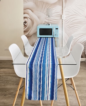 A dining table with a blue and white striped tablecloth, a microwave, and white chairs in a modern room with a floral wallpaper background. - Free Parking Newly Renovated New Kitchen 4th FL (Honolulu)