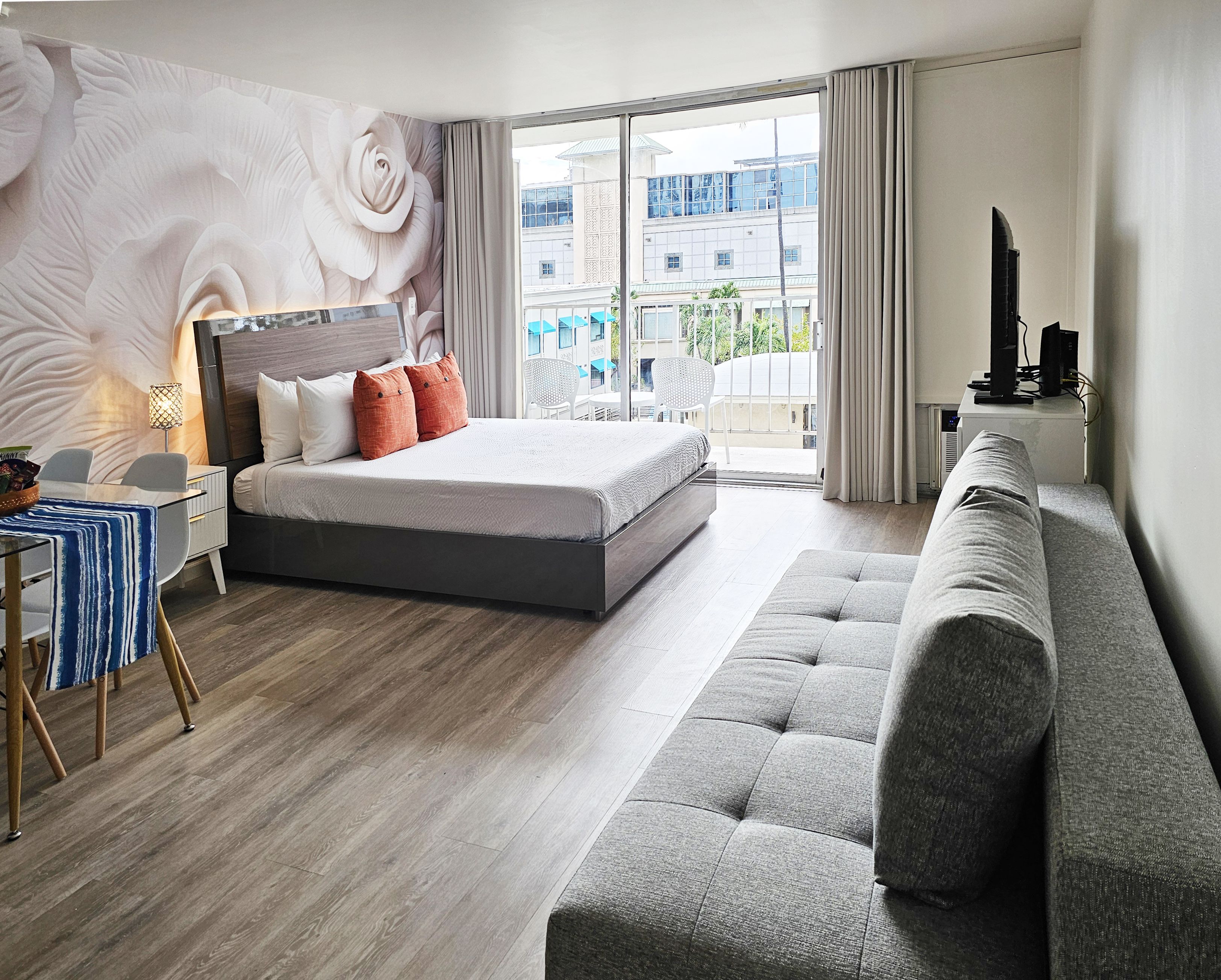 A modern hotel room with a large bed, a sofa, a desk with a lamp, and a view of the city through the window.