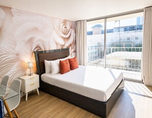 A modern hotel room with a large bed, a nightstand, a desk, and a view of the city through large windows. - Free Parking Newly Renovated New Kitchen 4th FL (Honolulu)