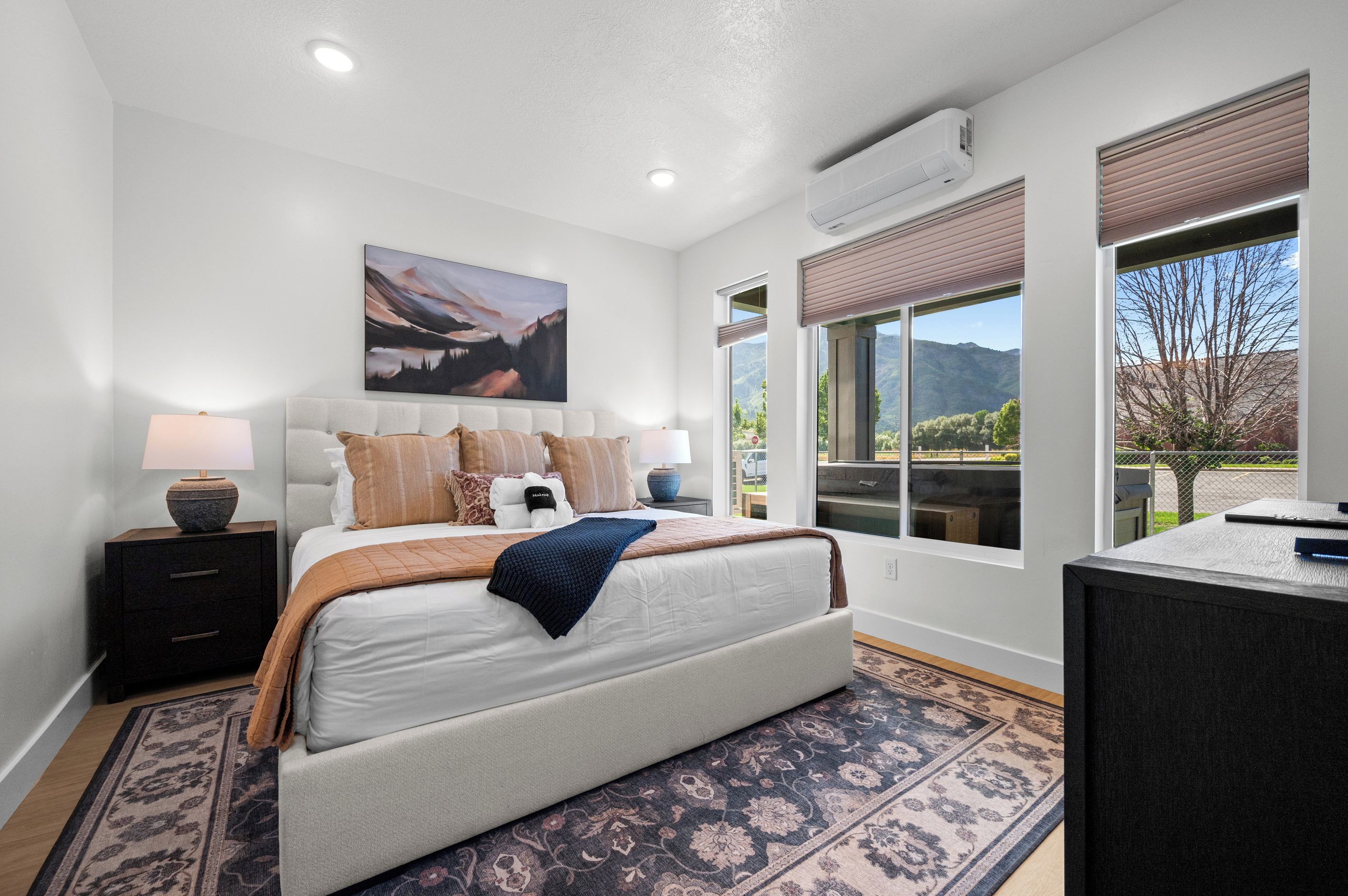 A bedroom with a bed, bedside lamps, a painting, and a view of the outdoors.