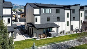 A modern multi-story residential building with a covered patio area and a view of mountains in the background. - Powderline Lodge | Hot Tub | 2 King Suites | Ski (Mountain Green)