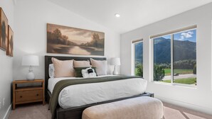 A bedroom with a bed, bedside tables, a painting, and a window with a mountain view. - Powderline Lodge | Hot Tub | 2 King Suites | Ski (Mountain Green)