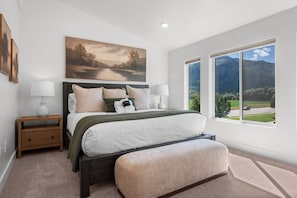 A bedroom with a bed, bedside tables, a painting, and a window with a mountain view. - Powderline Lodge | Hot Tub | 2 King Suites | Ski (Mountain Green)